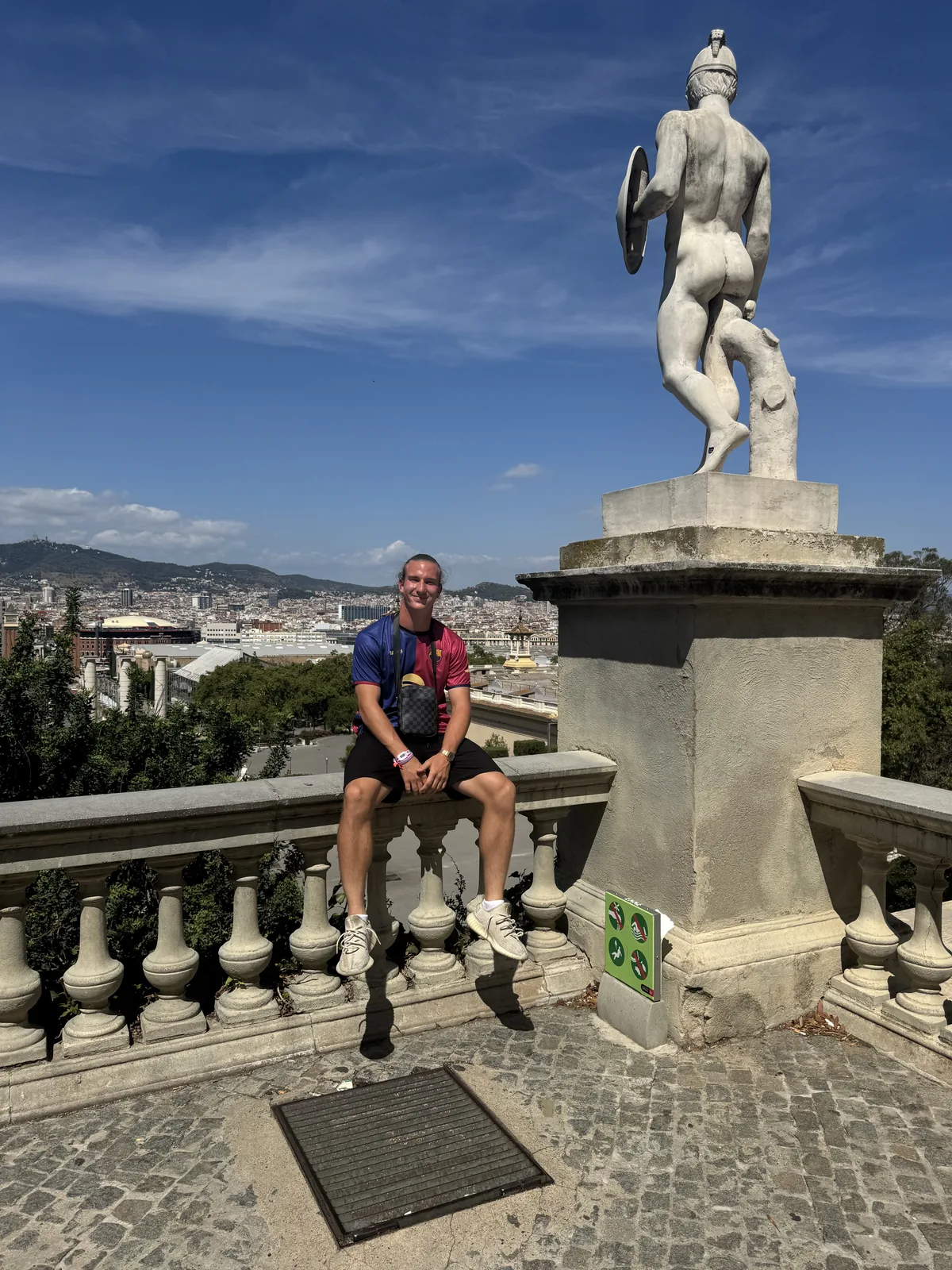 Ivan Vojvoda sjedi na kamenoj ogradi vidikovca s pogledom na Barcelonu i kip u pozadini
